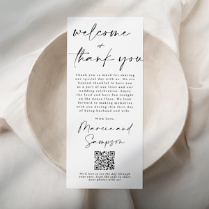 May include: A white wedding welcome sign with black calligraphy that reads "welcome + thank you". The sign also includes a QR code and the text "We'd love to see the day through your eyes. Scan the code to share your photos with us!"