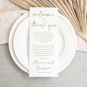 May include: A white wedding reception card with gold script that reads "welcome + thank you." The card includes a message of gratitude and well wishes, along with the names "Marcie and Sampson" and the date "October 13, 2029."