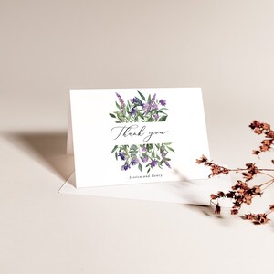 Op de afbeelding: Een witte gevouwen kaart met een aquarel bloemenontwerp. De kaart heeft paarse lavendel en groene bladeren, met de woorden "Thank you" in elegant schrift. De namen "Jessica and Henry" staan eronder gedrukt.