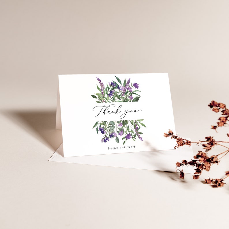 Op de afbeelding: Een witte gevouwen kaart met een aquarel bloemenontwerp. De kaart heeft paarse lavendel en groene bladeren, met de woorden "Thank you" in elegant schrift. De namen "Jessica and Henry" staan eronder gedrukt.