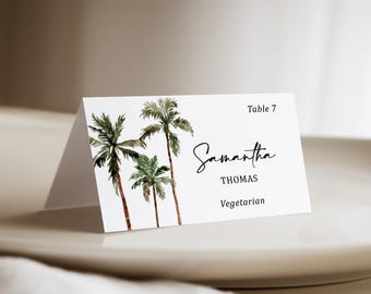 May include: A white folded place card featuring a watercolor illustration of three green palm trees on the left side. The text reads Table 7, Samantha, THOMAS, and Vegetarian in black ink, with a script font used for the name Samantha.