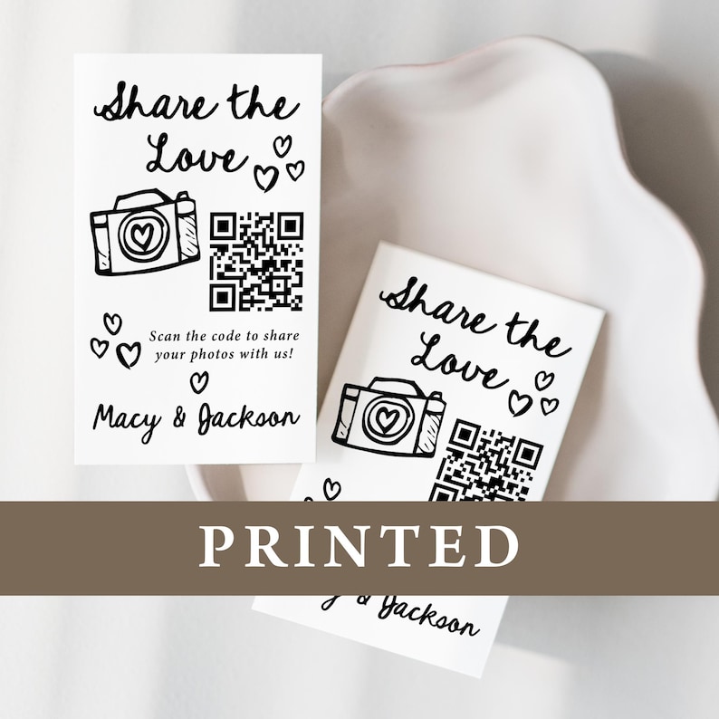 K&ouml;nnte beinhalten: Wei&szlig; bedruckte Karten mit dem Text "Share the Love" und einer Kamera-Grafik mit einem Herz. Enth&auml;lt einen QR-Code und die Namen "Macy & Jackson". Das Wort "PRINTED" ist ebenfalls sichtbar.