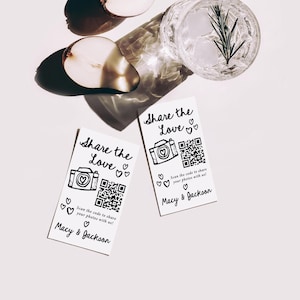 K&ouml;nnte beinhalten: Zwei wei&szlig;e Karten mit dem Text "Share the Love" und einer Kameraillustration. Jede Karte hat einen QR-Code und den Text "Scannen Sie den Code, um Ihre Fotos mit uns zu teilen!" und "Macy & Jackson". Ein Glas Wasser mit Eis und einem Rosmarinzweig ist sichtbar.