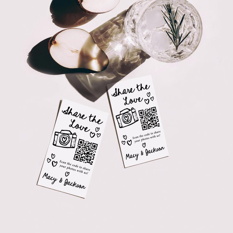 K&ouml;nnte beinhalten: Zwei wei&szlig;e Karten mit dem Text "Share the Love" und einer Kameraillustration. Jede Karte hat einen QR-Code und den Text "Scannen Sie den Code, um Ihre Fotos mit uns zu teilen!" und "Macy & Jackson". Ein Glas Wasser mit Eis und einem Rosmarinzweig ist sichtbar.