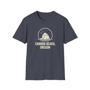 Peut inclure: Un t-shirt bleu marine avec un motif crème représentant une formation rocheuse, deux oiseaux et le texte "CANNON BEACH, OREGON". Le motif est centré sur le devant du t-shirt à manches courtes.
