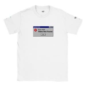 Op de afbeelding: Een wit T-shirt met korte mouwen en een grafische print van een computersysteemfoutvenster. Het venster toont een rood foutpictogram, de tekst 'System Error' en het bericht 'Error 404: Vibes Not Found' met een 'OK'-knop.