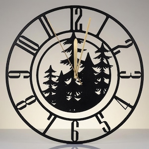 May include: A circular wall clock featuring a black metal frame with large cut-out numbers from one to twelve. The center of the clock displays a black silhouette of a pine forest. Two thin, gold-colored metal hands indicate the time.
