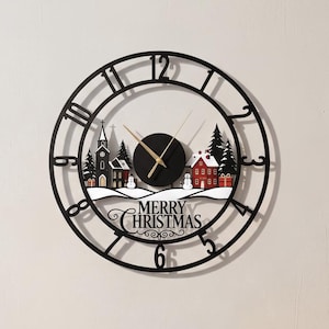 May include: A round black metal wall clock featuring a winter village scene with a church, a red house, snowmen, and pine trees. The clock face displays the text MERRY CHRISTMAS and has gold-colored hour and minute hands with black numerals.