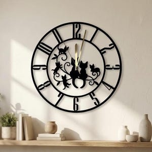 May include: A circular black wall clock featuring large cut-out numerals and a central decorative design of four cat silhouettes perched on swirling vine branches. The clock has two slender gold-colored hands indicating the time on the dial.