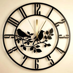 May include: A circular wall clock featuring a black open-frame design with large cut-out numerals. The centre displays a black silhouette of two birds perched on a leafy branch. The clock has thin, metallic gold-coloured hour, minute, and second hands.