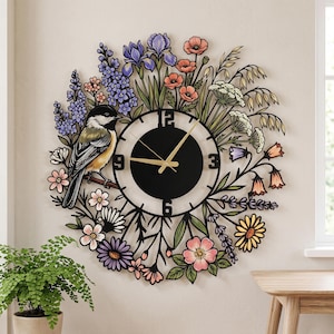 May include: A circular wall clock featuring a black center dial with gold hands and large black numerals at 3, 6, 9, and 12. The frame is decorated with a colorful metal cutout of a chickadee bird perched among various wildflowers.