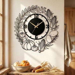 May include: A circular wall clock featuring a black center dial with gold hands and large black numerals at 12, 3, 6, and 9. The frame is a black metal cutout design depicting a harvest wreath with pumpkins, corn cobs, potatoes, and leafy branches.
