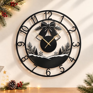 May include: A circular black wall clock featuring large cutout numerals from one to twelve. The center displays a decorative black bow, two bells, and a silhouette of pine trees over a snowy landscape. The clock has thin gold-colored hands.