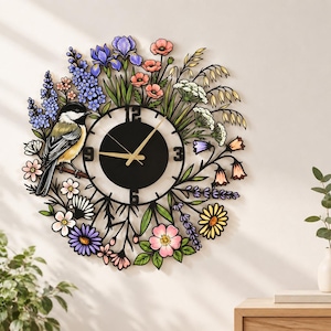 May include: A round wall clock featuring a black center dial with gold hands and numerals 3, 6, 9, and 12. The frame is decorated with a colorful array of wildflowers, lavender, and a black-capped chickadee perched on a branch on the left side.