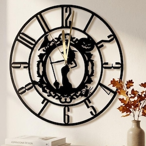 Peut inclure: Une horloge murale circulaire noire présentant un motif découpé représentant une sorcière tenant un balai, une citrouille d'Halloween et une araignée. L'horloge possède de grands chiffres noirs et des aiguilles dorées fines au centre.