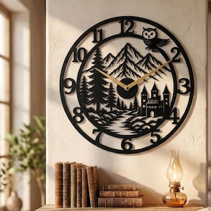 May include: A circular black wall clock featuring a laser-cut design of a mountain range, pine trees, a castle, and an owl. The clock face displays large black Arabic numerals and two thin gold-colored hands centered on the dial.