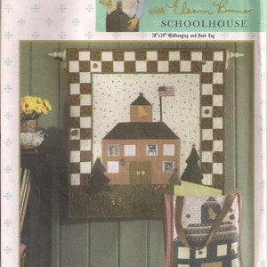 May include: A Simplicity Quilt in a Day pattern for a schoolhouse wallhanging and book bag. The pattern features a brown and white checkered border, a brown schoolhouse with a yellow star and a red, white, and blue American flag, and a book bag with a schoolhouse design. The pattern is titled "Schoolhouse" and includes the text "Quilt in a Day" and "Eleanor Burns".
