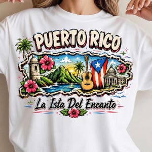 May include: A white t-shirt featuring a graphic of Puerto Rico with the text "PUERTO RICO" and "La Isla Del Encanto". The design includes a tropical landscape, a guitar, the Puerto Rican flag, hibiscus flowers, a fort, and a building.