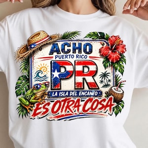 May include: A white t-shirt featuring a graphic design with a straw hat, a frog wearing sunglasses, a red hibiscus flower, and a coconut. The text reads ACHO PUERTO RICO PR LA ISLA DEL ENCANTO ES OTRA COSA, with the letters PR filled with the Puerto Rican flag.