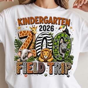 Puede incluir: Una camiseta blanca con un gráfico colorido y el texto KINDERGARTEN 2026 ZOO FIELD TRIP. El diseño incluye una jirafa, un elefante, un león, una cebra y un tucán integrados en los números, rodeados de hojas verdes y huellas de animales.
