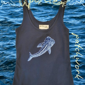 May include: A dark gray tank top featuring a white embroidered whale shark graphic on the front. The text "upcycled" is written in yellow at the top, and "patchwork" is written in yellow vertically along the right side of the garment.
