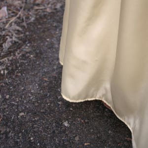 Peut inclure: Gros plan sur un tissu jaune p&acirc;le et fluide avec un l&eacute;ger &eacute;clat. Le bord du tissu est visible, avec une d&eacute;licate bordure de couleur claire. Le tissu est drap&eacute; en douceur, sugg&eacute;rant un v&ecirc;tement ou un textile.