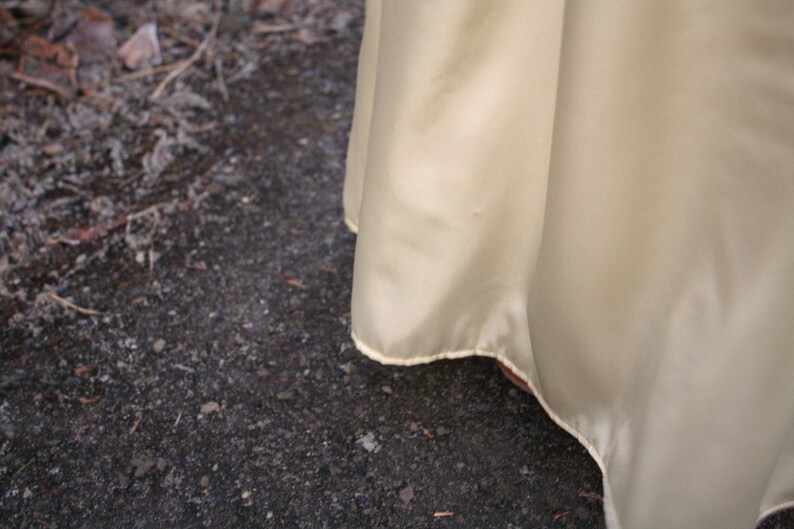 Peut inclure: Gros plan sur un tissu jaune p&acirc;le et fluide avec un l&eacute;ger &eacute;clat. Le bord du tissu est visible, avec une d&eacute;licate bordure de couleur claire. Le tissu est drap&eacute; en douceur, sugg&eacute;rant un v&ecirc;tement ou un textile.