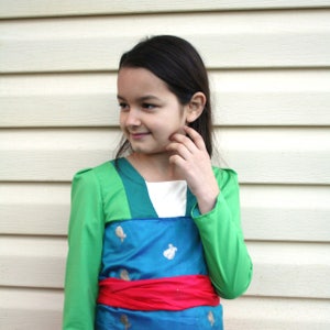 Peut inclure: Robe de costume verte et bleue avec des manches longues et une ceinture rouge. La robe a des accents dor&eacute;s et une encolure blanche. Le costume est port&eacute; par une personne aux cheveux fonc&eacute;s.