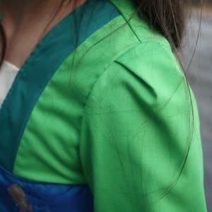 Peut inclure: Gros plan sur un v&ecirc;tement vert et bleu. La manche est vert vif, avec une bordure verte plus fonc&eacute;e sur l'&eacute;paule. Un panneau blanc et bleu est visible pr&egrave;s de l'encolure. Le tissu semble lisse, peut-&ecirc;tre satin&eacute;.