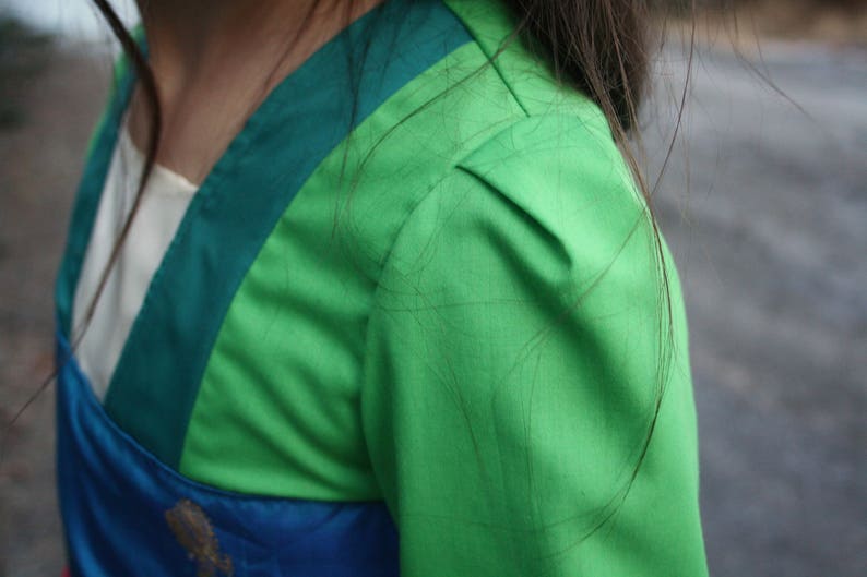 Peut inclure: Gros plan sur un v&ecirc;tement vert et bleu. La manche est vert vif, avec une bordure verte plus fonc&eacute;e sur l'&eacute;paule. Un panneau blanc et bleu est visible pr&egrave;s de l'encolure. Le tissu semble lisse, peut-&ecirc;tre satin&eacute;.