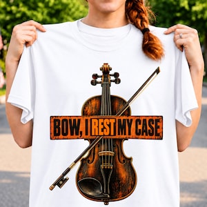 Könnte beinhalten: Ein weißes T-Shirt mit einer Grafik einer braunen Holzgeige und einem Bogen. Über die Mitte verläuft ein orangefarbenes rechteckiges Banner mit dem schwarzen Text "BOW, I REST MY CASE". Die Geige hat ein dunkles, verwittertes Finish mit sichtbaren Saiten.