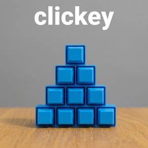 Op de afbeelding: Een piramidevormige stapel van tien blauwe vierkante mechanische toetsenbordtoetsen gerangschikt in vier rijen, met het woord "clickey" in witte letters boven de stapel. De toetsen hebben een matte afwerking en een verhoogd vierkant ontwerp.