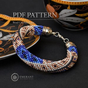 May include: A bead crochet rope bracelet featuring a geometric pattern in shades of blue, beige, black, and white. The bracelet has silver-toned metal end caps and a lobster claw clasp. The text PDF PATTERN Bead Crochet Rope is visible.