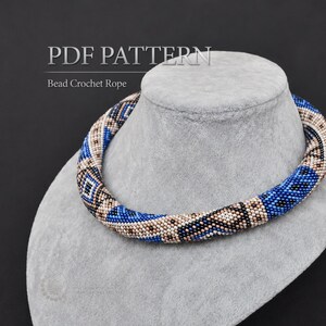 May include: A bead crochet rope necklace featuring a geometric pattern in shades of blue, beige, black, and white. The text PDF PATTERN Bead Crochet Rope is displayed above the necklace. The jewellery is displayed on a grey velvet display bust.