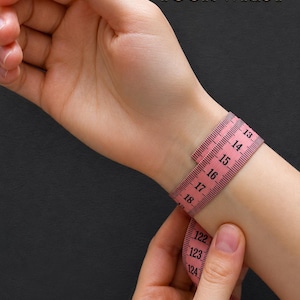 May include: A pink measuring tape wrapped around a wrist with the text HOW TO MEASURE YOUR WRIST and the logo EMERANT BEAD CROCHET PATTERS. The tape shows numerical markings in centimetres, with the visible range spanning from 13 to 124.