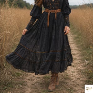 May include: A long-sleeved black dress featuring a tiered skirt with brown stitching details, a button-up bodice with lace accents, and a brown leather belt with a metal buckle, paired with brown lace-up leather boots.
