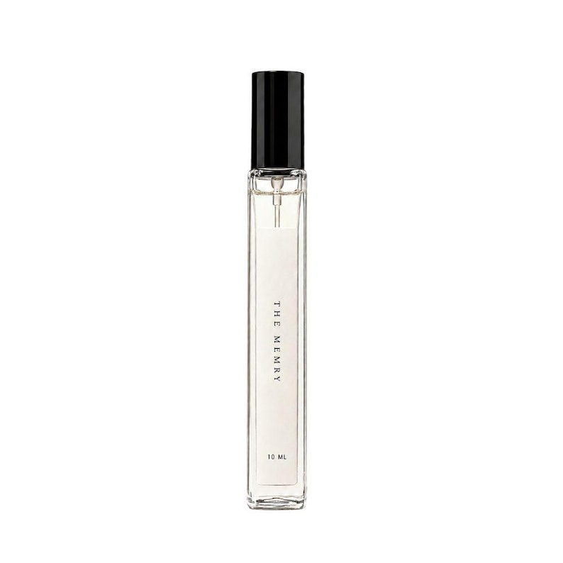 May include: A tall, slender, clear glass perfume bottle with a black cylindrical cap and a spray nozzle. The white label on the front features the text THE MEMRY and 10 ML in black font. The bottle contains a clear liquid and has a rectangular shape.
