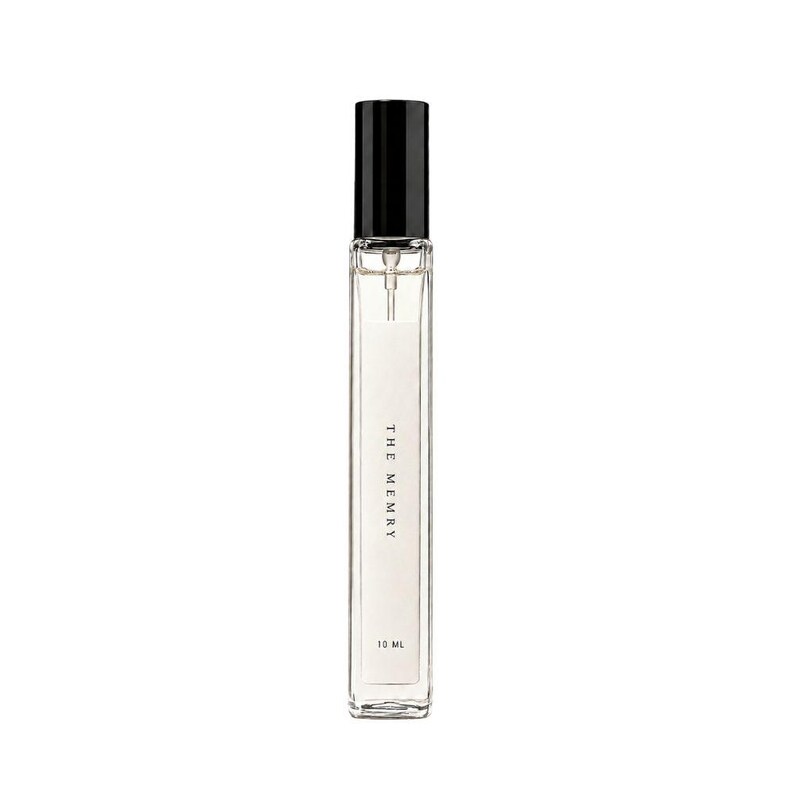 May include: A tall, slender, clear glass perfume bottle with a black cylindrical cap and a spray nozzle. The white label on the front features the text THE MEMRY and 10 ML in black font. The bottle contains a clear liquid and has a rectangular shape.