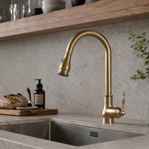Peut inclure: Un robinet de cuisine en or brossé avec un bec col de cygne à arc élevé et une douchette extractible. Le robinet dispose d'une poignée latérale unique pour le contrôle de l'eau et d'une finition métallique, placé au-dessus d'un évier en inox.