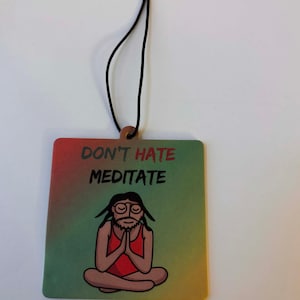 Może przedstawiać: Kwadratowy odświeżacz powietrza z napisem "DON'T HATE MEDITATE" nad kresk&oacute;wkową ilustracją medytującej osoby. Odświeżacz powietrza ma gradientowe tło w kolorach czerwonym, zielonym i ż&oacute;łtym. Do zawieszenia przymocowany jest czarny sznurek.