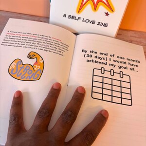 May include: A self-love zine with the text "A SELF LOVE ZINE" on the cover. The open pages show text and a calendar graphic. The text includes the phrase "By the end of one month (30 days) I would have achieved my goal of..."