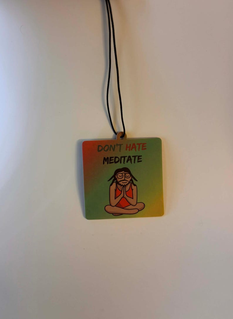 Może przedstawiać: Kwadratowa drewniana ozdoba z czarnym sznurkiem. Ozdoba ma gradientowe tło w kolorach czerwonym, ż&oacute;łtym i zielonym. Tekst "DON'T HATE MEDITATE" jest wydrukowany nad postacią z kresk&oacute;wki w pozycji jogi.