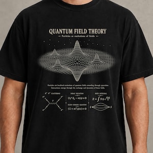 Puede incluir: Una camiseta negra con un estampado gráfico blanco de una cuadrícula de teoría cuántica de campos con picos y valles. El texto dice QUANTUM FIELD THEORY, Particles as excitations of fields e incluye ecuaciones físicas.