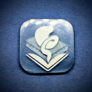 Puede incluir: Un colgante cuadrado azul claro con un diseño blanco estilizado de caduceo. El caduceo, símbolo de la medicina, está compuesto por un bastón, serpientes y alas, sobre un fondo de libros. El colgante tiene una superficie ligeramente texturizada.