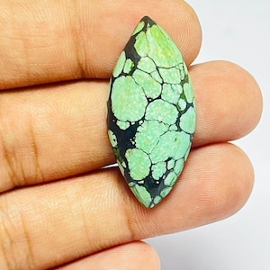 Può includere: Una pietra preziosa turchese a forma di marquise caratterizzata da un vibrante colore verde chiaro con una prominente trama a matrice nera scura che attraversa l'intera pietra. La superficie è liscia e lucida, con un motivo naturale di venature.