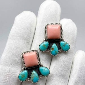 May include: A pair of earrings featuring a central square pink stone set in silver, surrounded by three teardrop-shaped turquoise stones at the base. The metal settings have a twisted rope texture around the edges of the square stones.