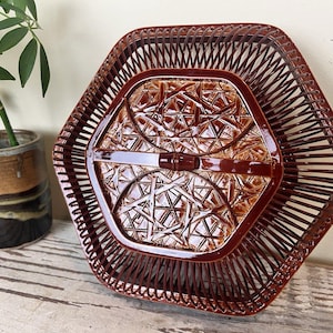 May include: A hexagonal brown ceramic basket with a glossy finish. The structure features a cage-like design with thin, vertical slats surrounding a central, raised panel that displays an intricate, woven-style relief pattern in shades of brown.