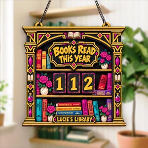 May include: A rectangular wooden hanging sign with a black and gold bookshelf design. The text reads BOOKS READ THIS YEAR and LUCIE'S LIBRARY. The center features the number 112 on three cards. The shelves are decorated with colorful books and pink roses.