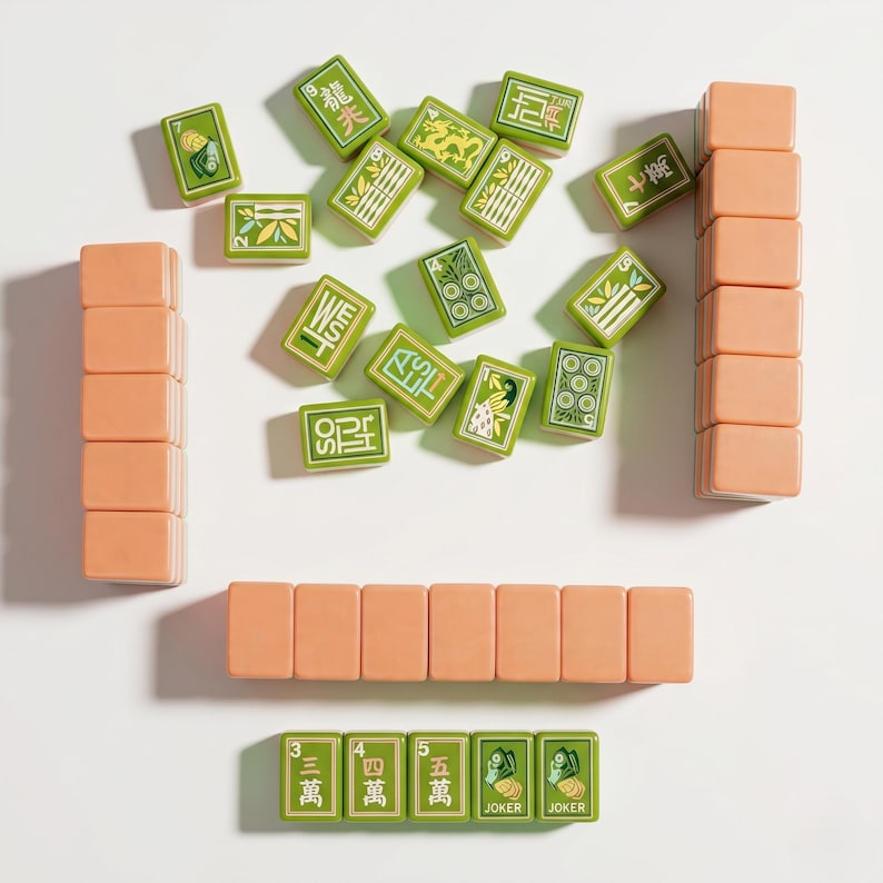 May include: A set of mahjong tiles including several peach-colored blank tiles arranged in stacks and rows, alongside green tiles featuring various symbols, numbers, Chinese characters, and the word JOKER printed in white, black, and gold ink.