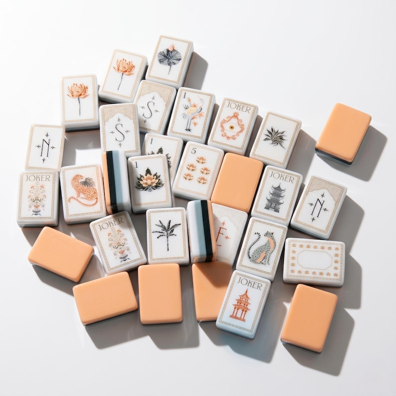 May include: A collection of rectangular mahjong tiles featuring a mix of solid peach-colored backs and white faces decorated with intricate illustrations of flowers, leopards, pagodas, and the word Joker in black, orange, and muted green ink.